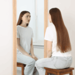 Woman looking in the mirror at herself looking unhappy due to body dysmorphic disorder in adults