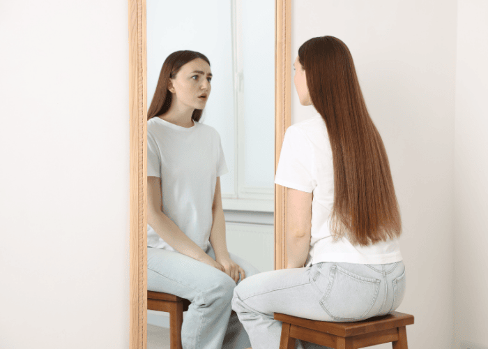 Woman looking in the mirror at herself looking unhappy due to body dysmorphic disorder in adults