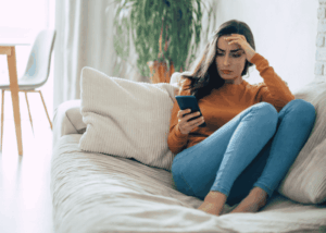 Woman sitting on the couch looking at her phone, struggling with social media and depression