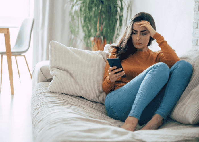 Woman sitting on the couch looking at her phone, struggling with social media and depression in adults