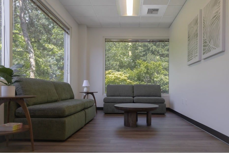 Minimalist therapy room with green sofas and large windows showing a natural forest view.