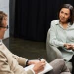 cognitive behavioral therapy being conducted between a male therapist and a female patient while the therapist takes notes on cbt skills
