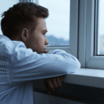Man feeling sad looking out the window, in need of separation anxiety disorder treatment