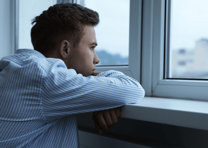 Man feeling sad looking out the window, in need of separation anxiety disorder treatment