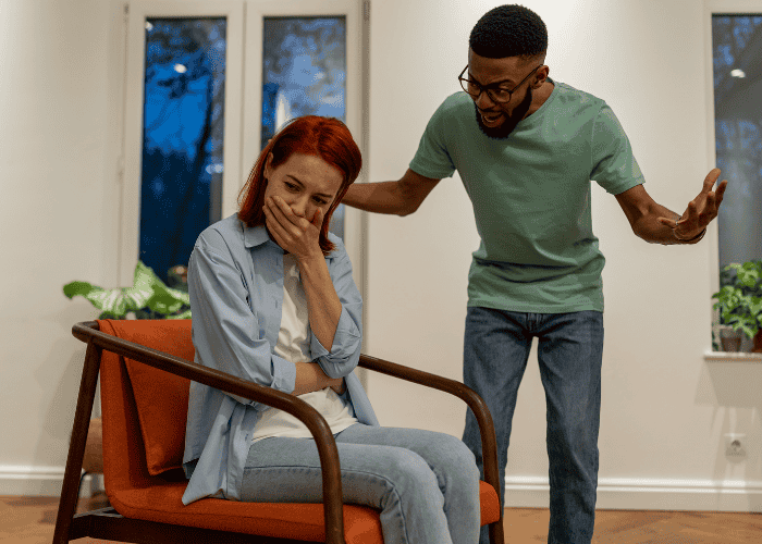 Man shouting at woman while she sits with her hand over her mouth, in need of psychological abuse trauma treatment