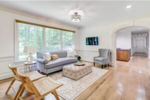 A bright, welcoming therapy office of AMFM with a gray sofa, a wingback chair, and large windows.