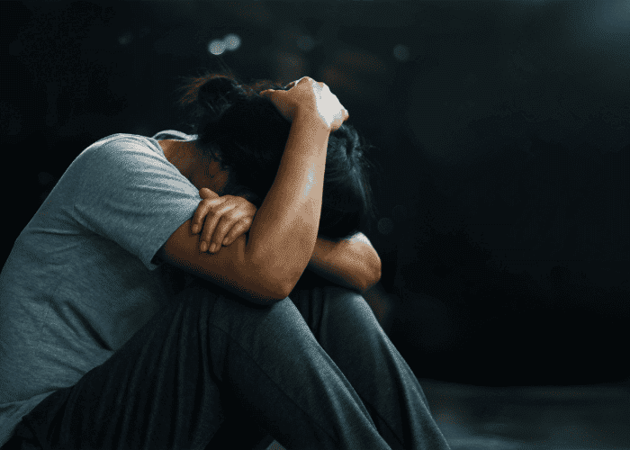 Woman in a dark room with her knees to her chest and hand on her head due to lack of California digital safety laws