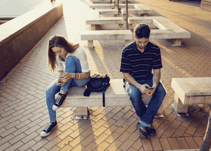 Two people sitting on a bench typing on chatbots for mental health