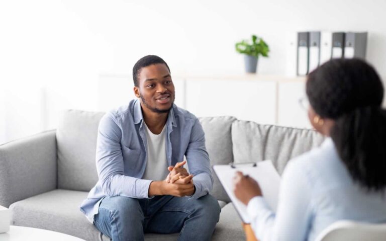 Man sitting on sofa looking at female therapist during mental health treatment therapy session