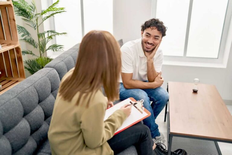 Man and woman sitting on couch looking at each other while woman takes notes on her clipboard