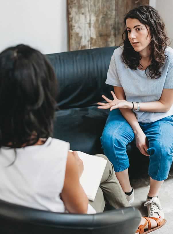 Woman wearing jeans and a t-shirt sitting on couch across from therapist during therapy appointment