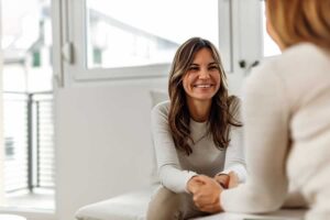Woman smiling while sitting across from and looking at her female therapist