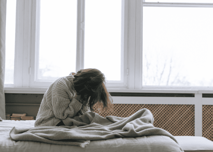 Woman sitting in bed with her head in her hands managing chronic pain