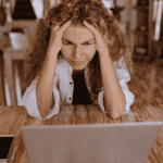 Woman looking frustrated at her laptop due to AI in mental health treatment