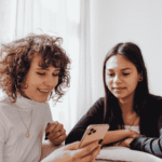 Two women sitting next to each other looking at one woman's cell phone for answers
