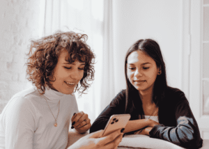Two women sitting next to each other looking at one woman's cell phone for answers