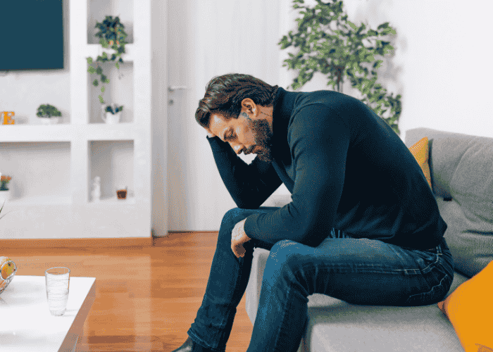 Man sitting on the sofa with his head in his hands wondering when to seek professional help