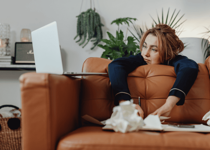 Woman leaning over her sofa looking at her laptop, dealing with burnout vs depression