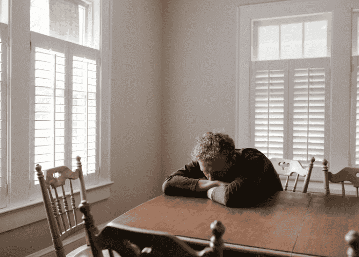 Man with his head down on his dining room table, struggling with burnout vs depression