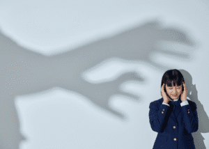 Woman with her hands over her ears with a shadow of hands on the wall, representing news anxiety
