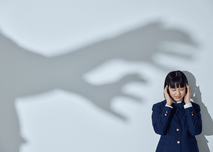 Woman with her hands over her ears with a shadow of hands on the wall, representing news anxiety