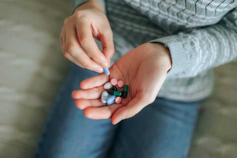 Ariel view close up of hands holding various prescription pills in one palm while person sits on couch