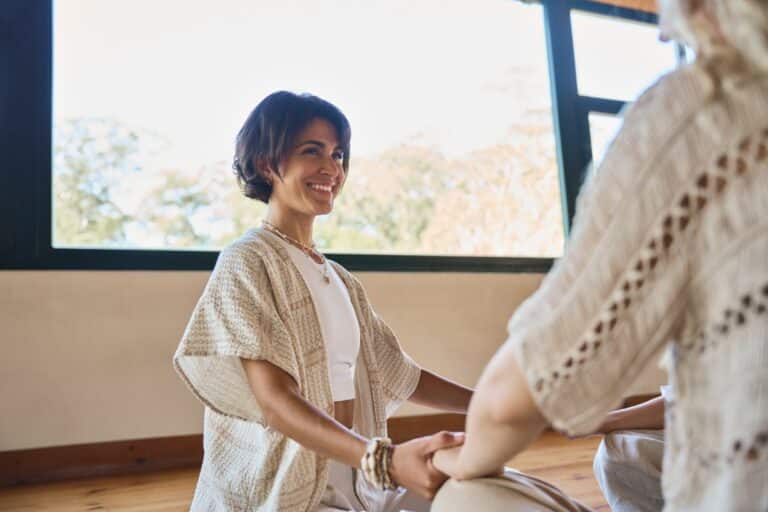 Woman with short hair sitting on the ground cross legged smiling as she practices yoga