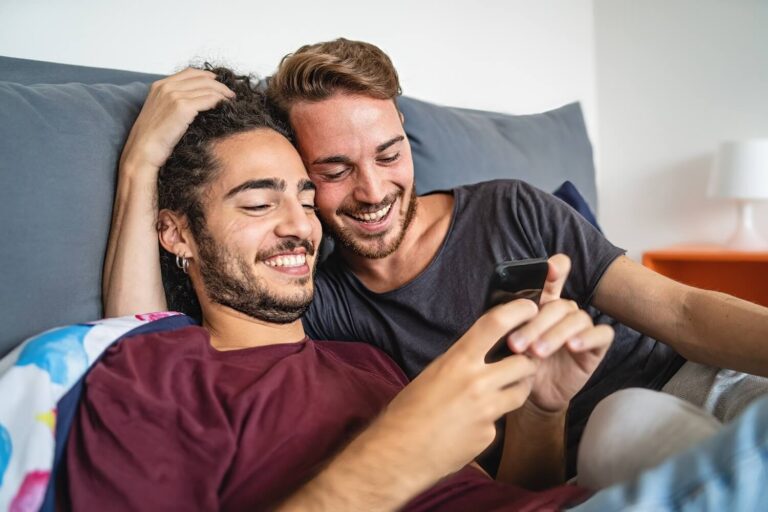 Male couple snuggling while looking at phone and smiling