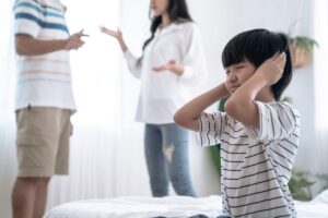 Child standing up covering his ears while his parents argue behind him