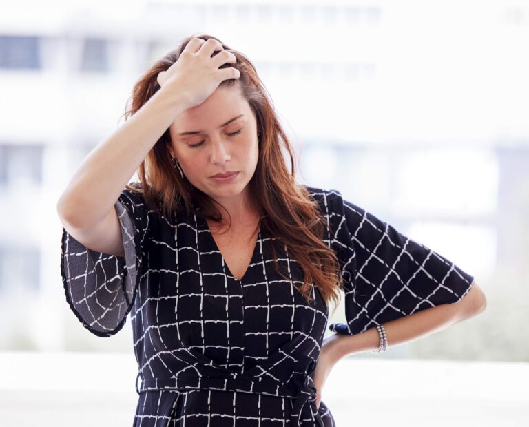 Woman looking frustrated with eyes closed and one hand on hip while other hand is on head