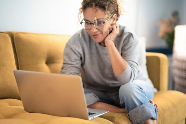 Woman sitting on sofa looking at her laptop with smile on her face