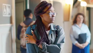 Female college student standing in hallway looking worried and uncomfortable