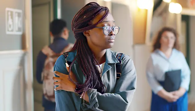 Female college student standing in hallway looking worried and uncomfortable